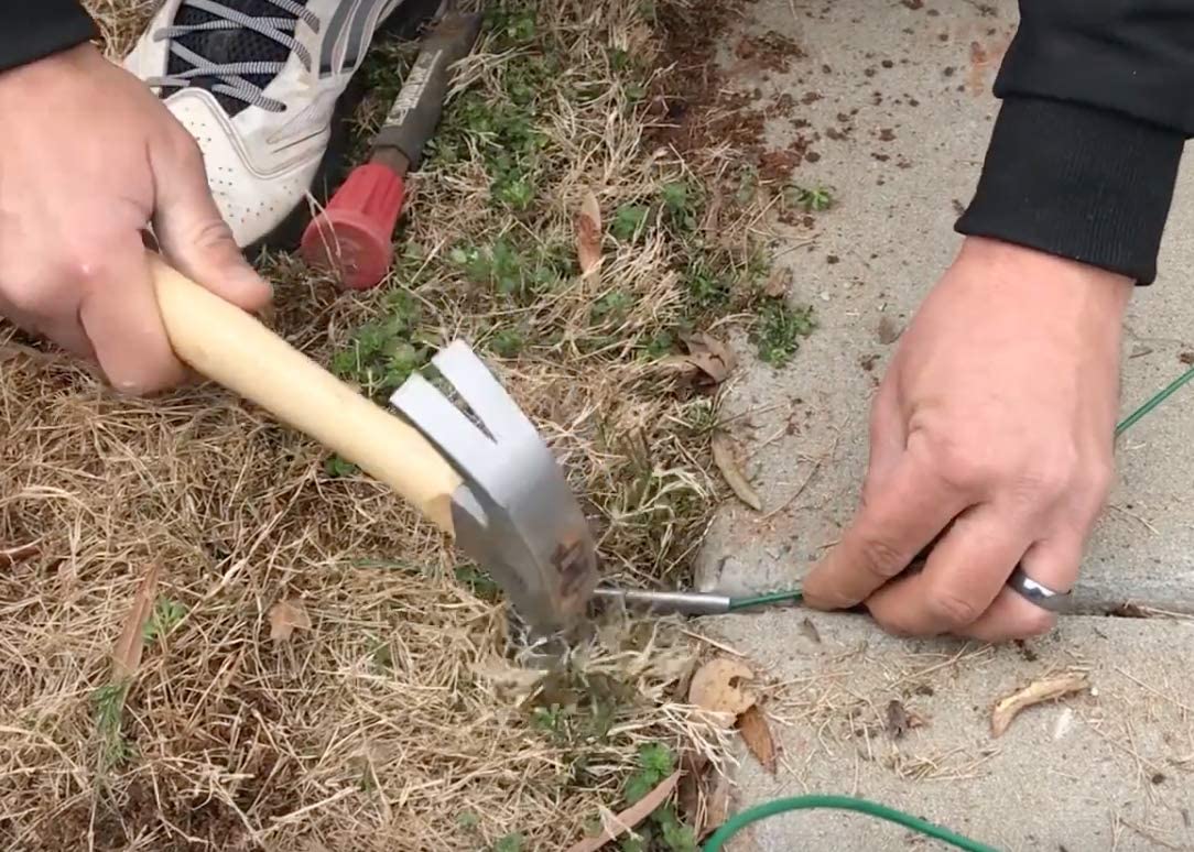 Hands installing wiresaver over wire using hammer to pound wiresaver in the ground