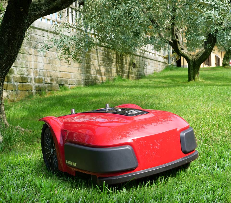Red Ambrogio L350i in foreground on grass, trees and wall on the left and in background
